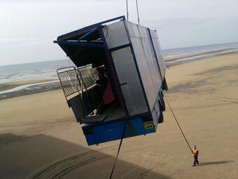 Amusement park structure being moved on the beach in Blackpool with a crane while a worker secures the transport
