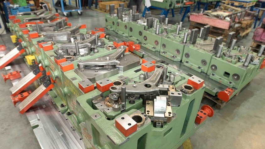Transferwerkzeug für Querlenkerarm – Werkzeugbau im Einsatz Transferwerkzeug für einen Querlenkerarm in der Automobilproduktion; komplexe Werkzeugaufspannung mit mehreren Formnestern und mechanischen Einheiten in der Werkhalle von weba Werkzeugbau.
