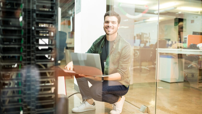 Mladý IT specialista pracuje s notebookem v moderním kancelářském prostředí vedle serverového racku.