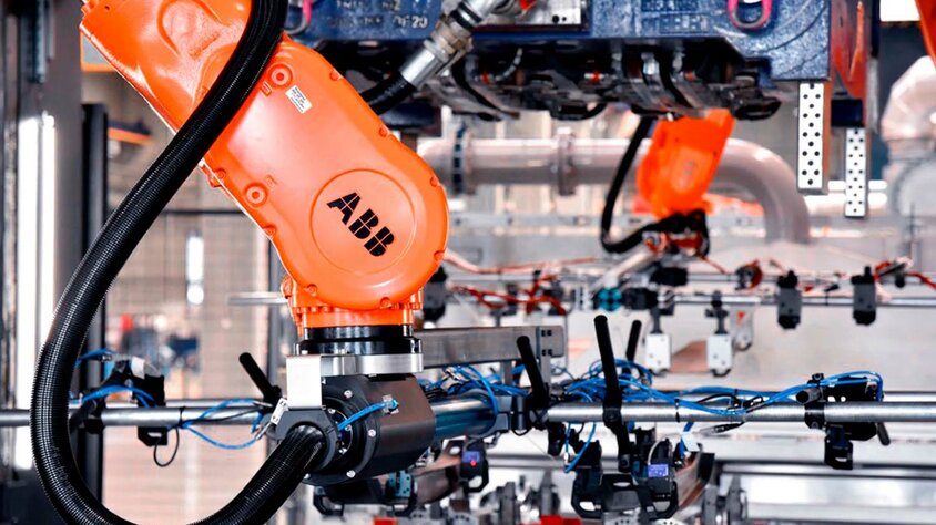  An industrial robotic arm in tool manufacturing, working on a complex production line. The orange ABB robotic arm is equipped with various gripping and sensor tools and is used in series production and forming technology. In the background, additional mechanical components and wiring are visible, highlighting the state-of-the-art automation and precision in manufacturing technology.