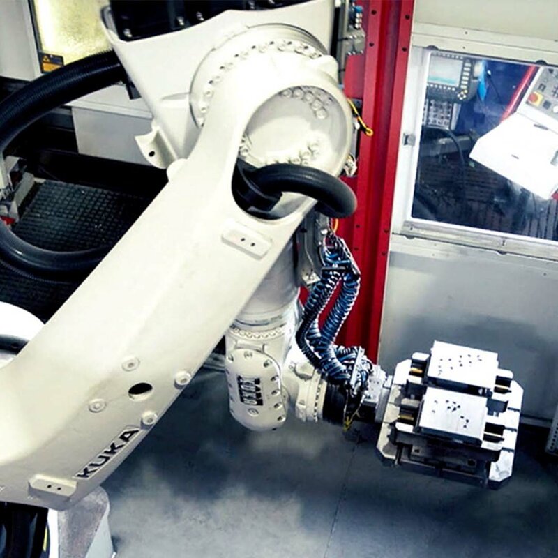 Ein Roboterarm eines automatisierten 5-Achs Bearbeitungszentrums für Einzelteilfertigung entnimmt Stahlblöcke aus dem Palettenwechsler.