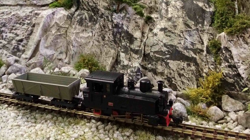 Schwarze Modell-Dampflokomotive mit Güterwagen vor einer detailreich gestalteten Felslandschaft.