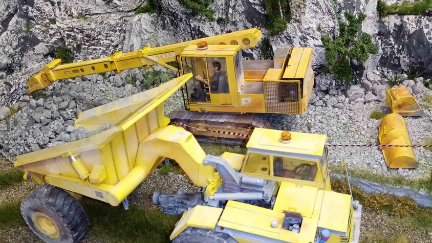 Detailreiche Modellbauszene mit gelben Baumaschinen vor einer felsigen Landschaft.