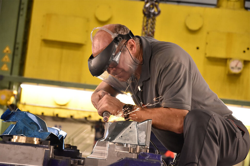Nástrojářský technik pracuje na nástrojové destičce v tvářecím lisu. Při bodování létají jiskry. Technik má na obličeji ochranný štít, který zajišťuje jeho bezpečnost během přesného a náročného pracovního procesu při zkoušení forem.