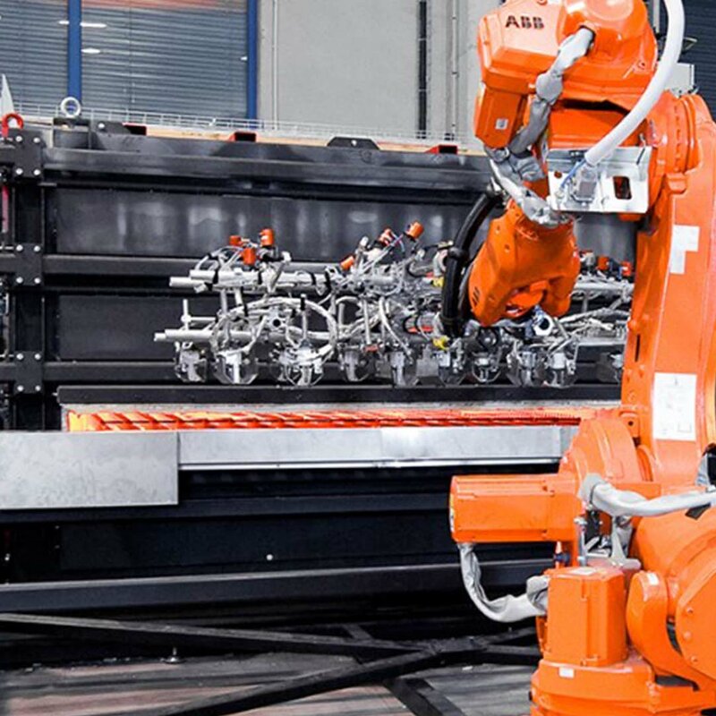 Ein Roboterarm entnimmt vier glühende Formplatinen aus einem Kammer-Warmformofen für den Transfer in die Umformpresse und Bauteilproduktion.