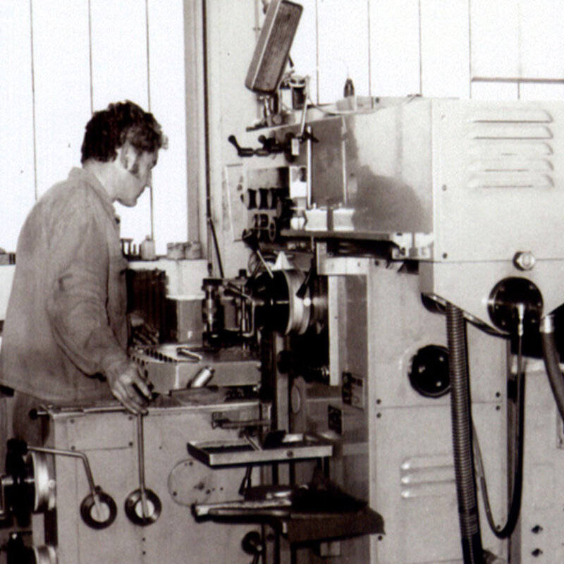 Ein Schwarz-Weiß-Bild aus den 80er Jahren zeigt einen Zerspanungstechniker, der ein konventionelles Bohrwerk bedient.