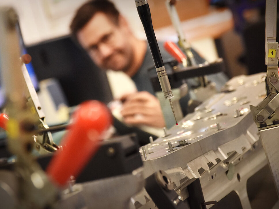 Detail souřadnicového měřicího stroje se zaměřením na měřicí sondu. V pozadí je vidět rozmazaný a rozostřený měřicí technik.