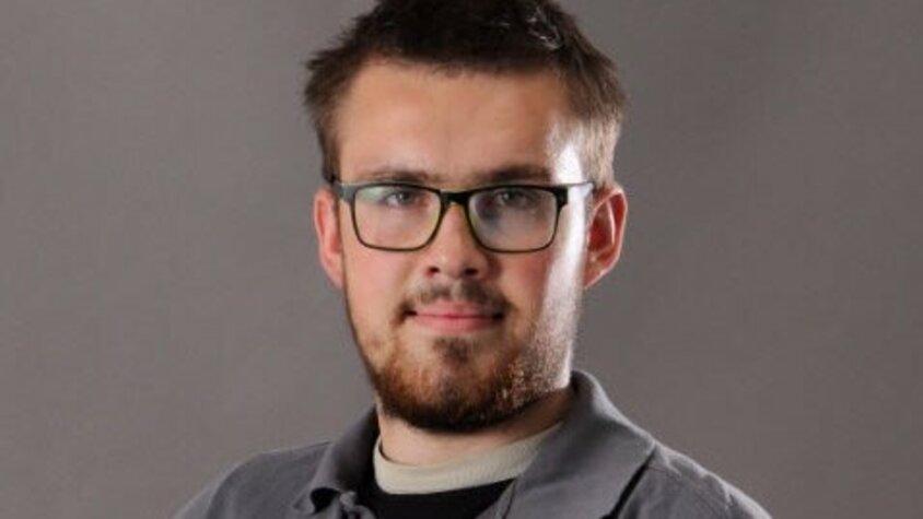 Porträt von Werkzeugmacher Jan Wengryn im grauen weba-Poloshirt, freundlich lächelnd vor neutralem Hintergrund.