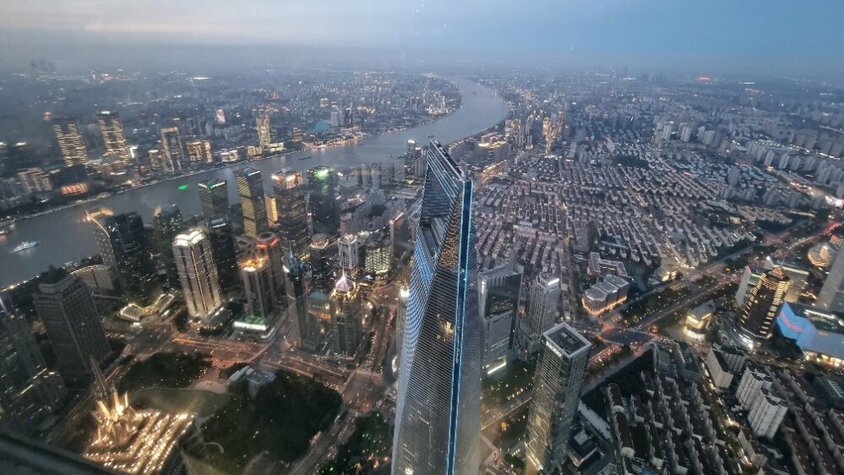 Blick aus luftiger Höhe auf die Skyline von Shanghai bei Dämmerung, mit dem Huangpu-Fluss und leuchtenden Wolkenkratzern – ein Moment aus Jan Wengryns Auslandseinsatz in China.