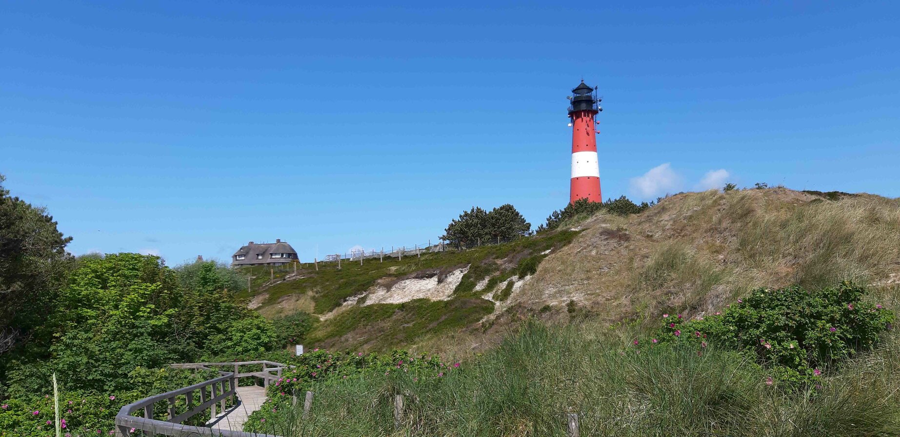 Red lighthouse on a dune landscape by the sea under a clear blue sky.