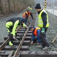 Několik členů klubu železničních modelářů společně pracuje na kolejích ve venkovním prostoru.