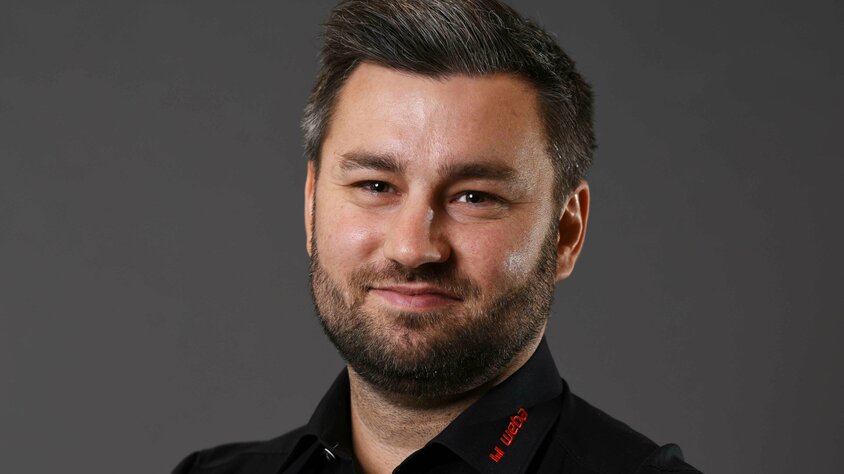weba Werkzeugbau Kubka Alexander präsentiert sich freundlich und professionell: schwarzes Hemd mit rotem weba-Logo, vor grauem Hintergrund, direkt in die Kamera lächelnd.