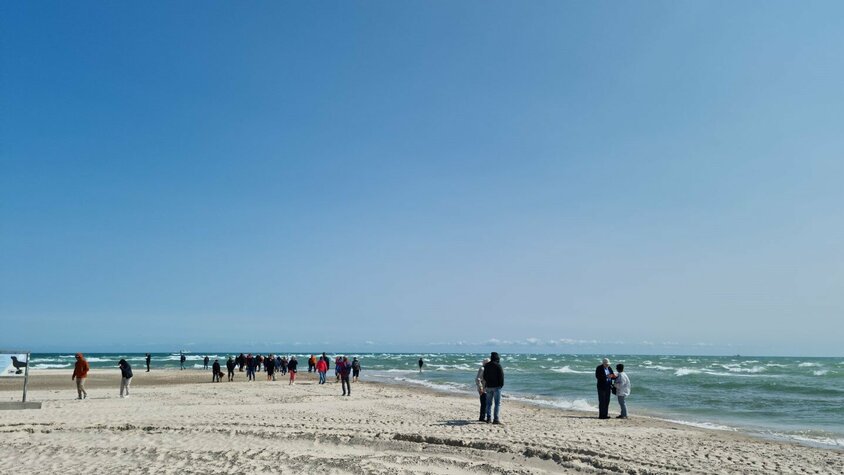 Strand in Dänemark Eine Gruppe von Menschen spaziert bei sonnigem Wetter an einem Sandstrand entlang, wo sich Nord- und Ostsee treffen. Der Himmel ist strahlend blau, das Meer leicht bewegt.